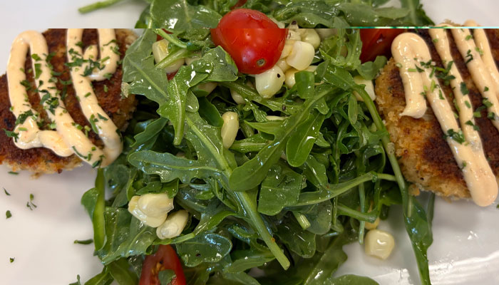 Arugula salad with cherry tomatoes, corn, and two breaded cakes from the Cafe Catron menu.
